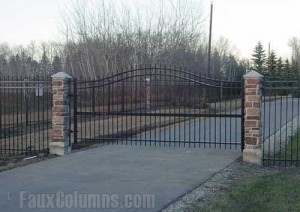 Wrought iron driveway gate flanked by two faux stone columns.
