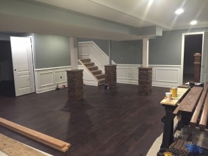 Finished basement with hardwood floors and support pillars wrapped in faux stacked stone.