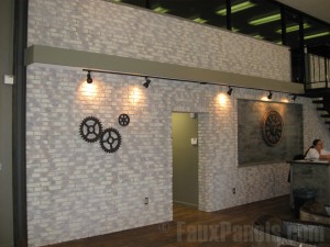 In addition to the faux brick accent wall, designers added an oversized Victorian inspired clock behind the desk and an industrial gear motif, both highlighted by the track lights overhead. A Victorian inspired clock & industrial gear motif add unique touches to the accent wall.