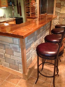 DIY wet bar island covered in cobblestone style panels and framed with natural wood.
