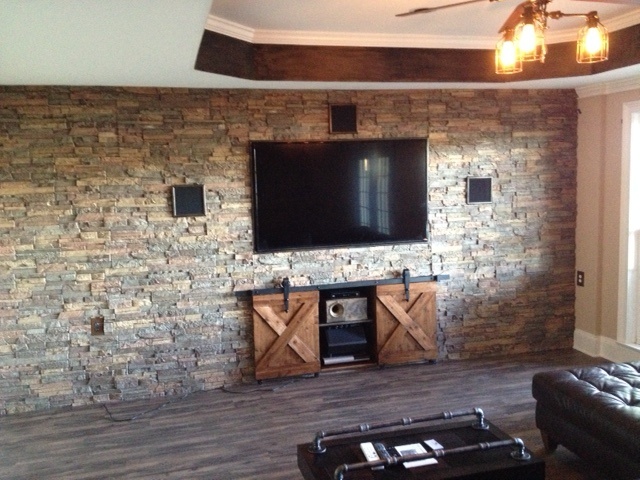 Basement TV wall covered with faux dry stack stone panels and mini barn doors.