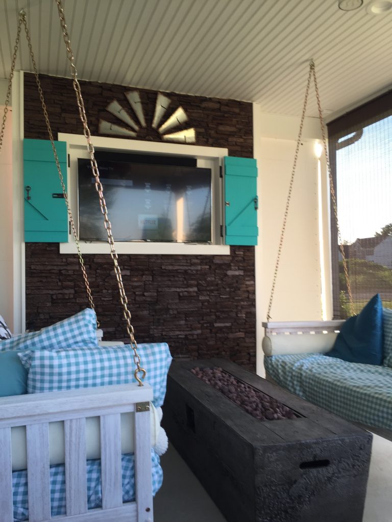 Newly built enclosed patio with swing seating and TV mounted on a faux stacked stone accent wall.