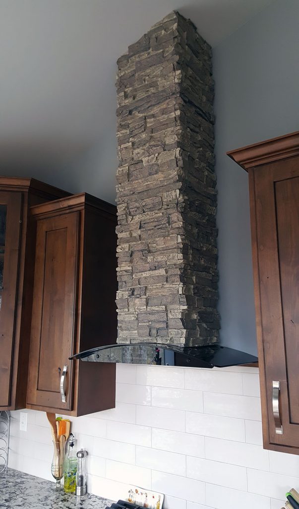 DIY range hood covered by a stacked stone column wrap.
