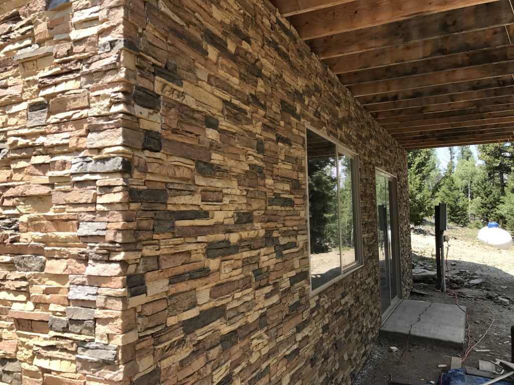 Finishing exterior foundation walls of a log cabin with Norwich Stacked Stone panels in Desert Sand color