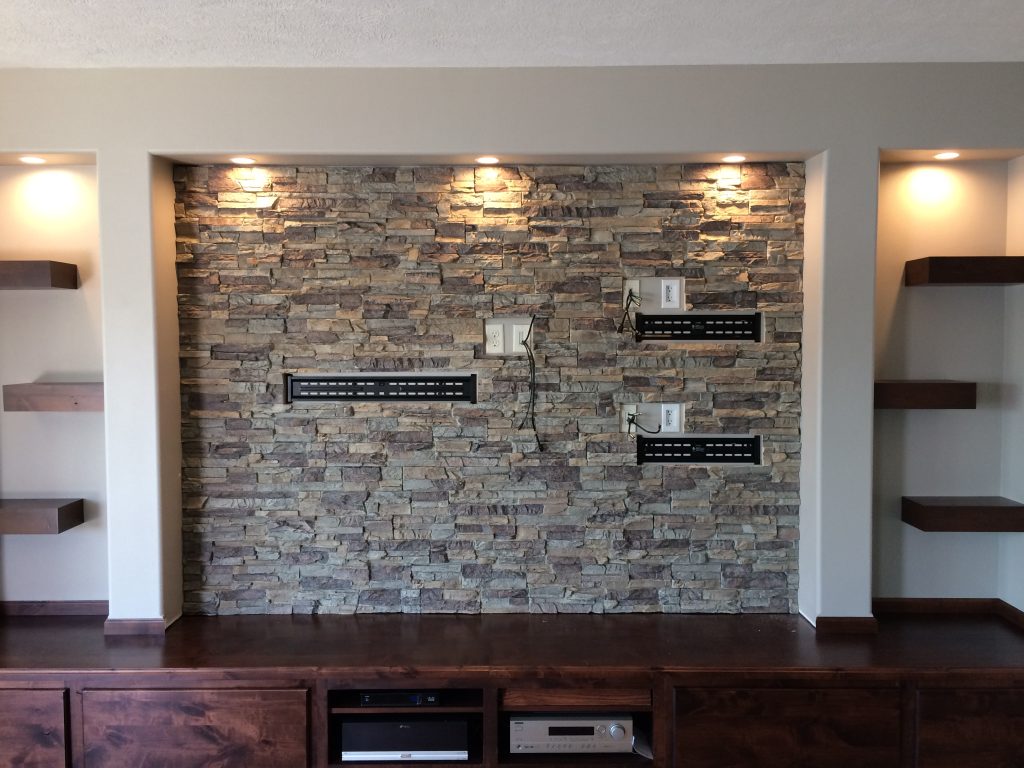 Media center finished with stone style wall panels with holes cut out to accommodate mounting brackets.