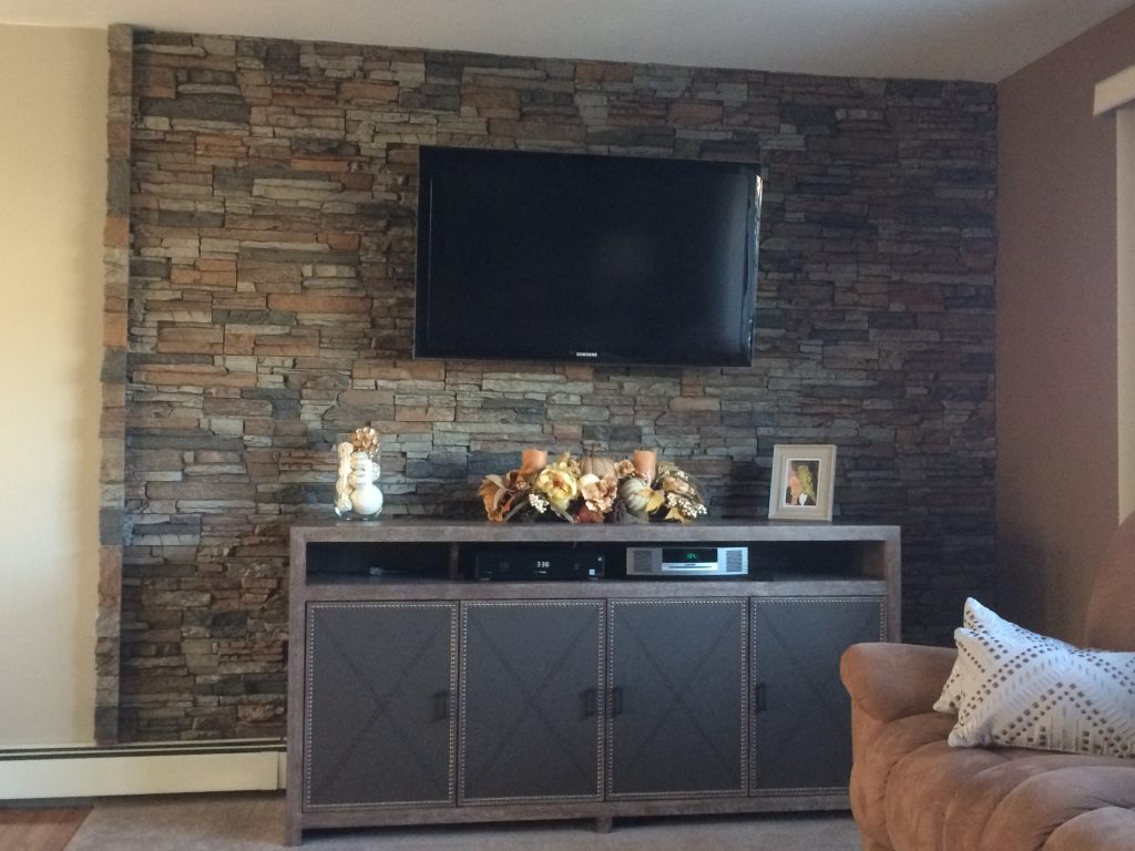 A living room's accent wall created with stacked stone panels behind the TV.