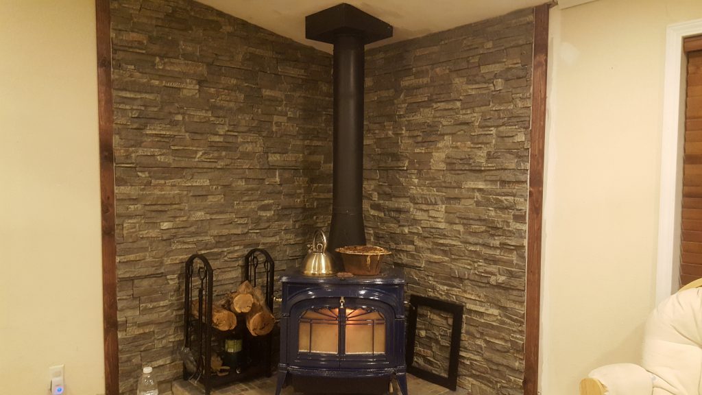 Wall behind a wood stove created with stacked stone style panels.