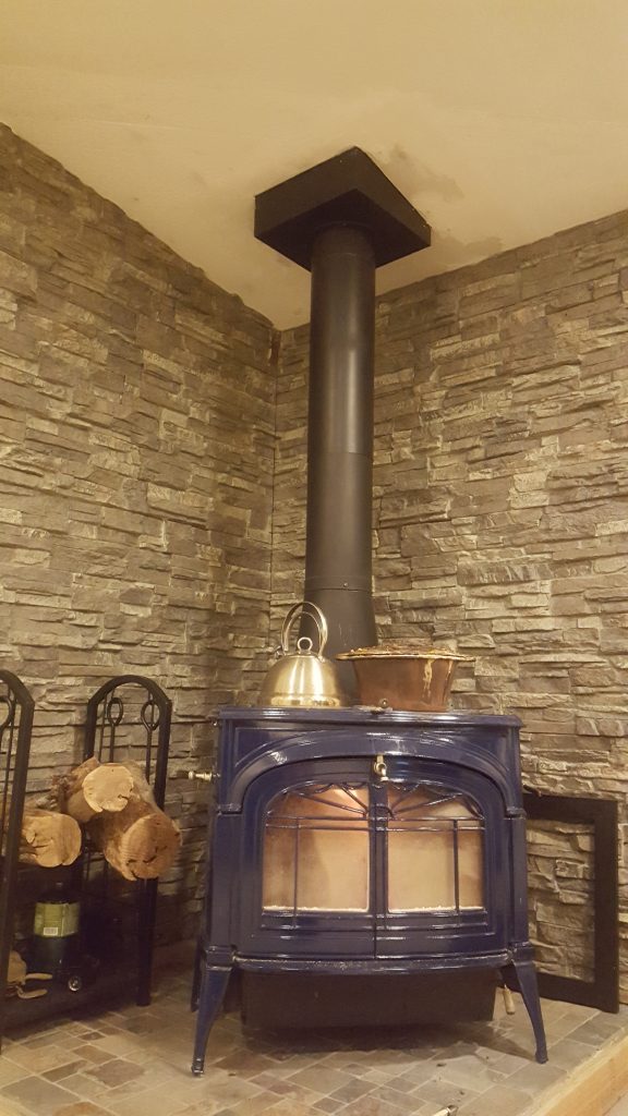 Close-up view of Franklin wood stove with a new stacked stone paneled wall behind it.
