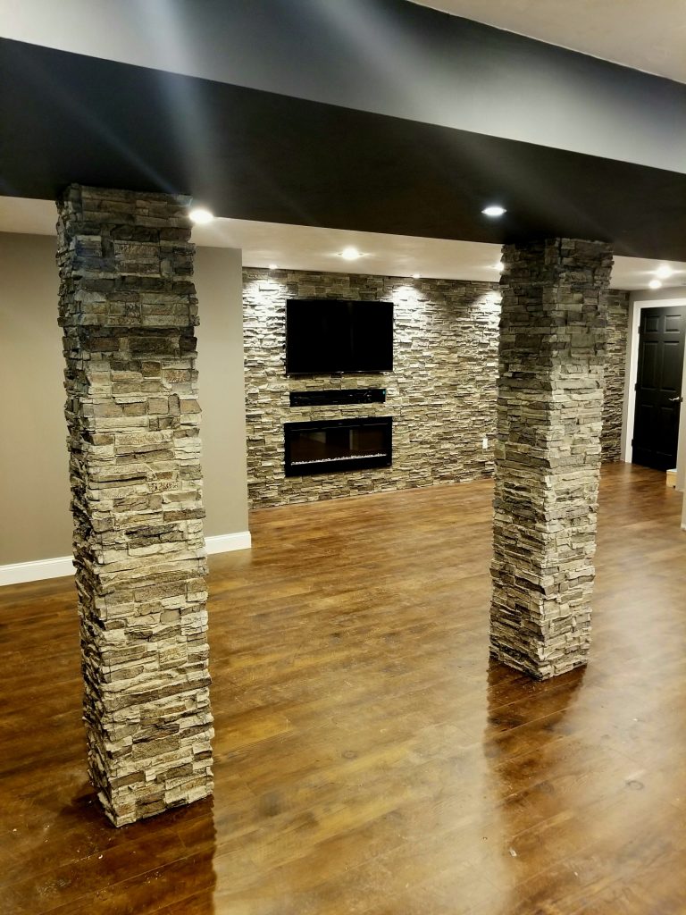 New basement accent wall with TV and fireplace and lally columns covered in Norwich Stacked Stone panels and matching column wraps.