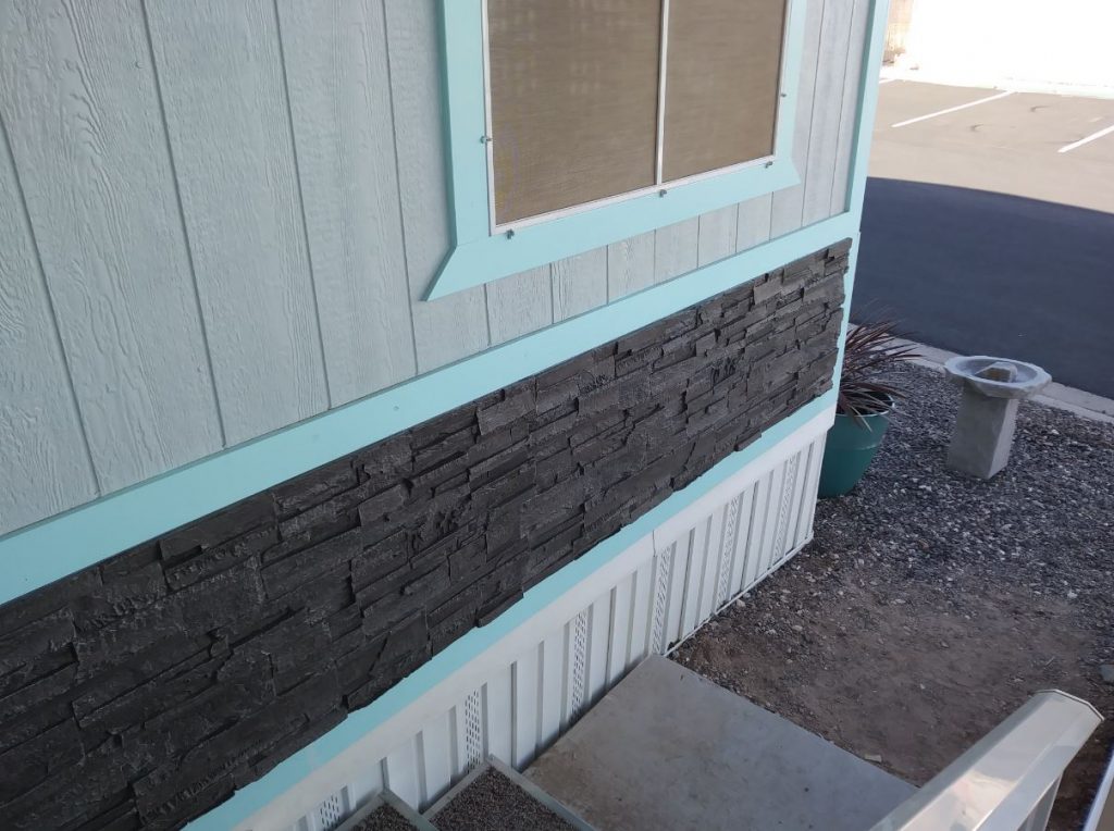 Mobile home with stone texture panels, white paneled foundation and eggshell blue trim.