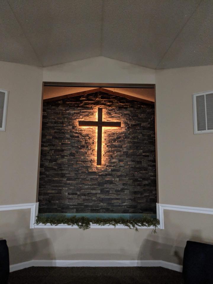 Illuminated cross installed over stacked stone panels in a church sanctuary.