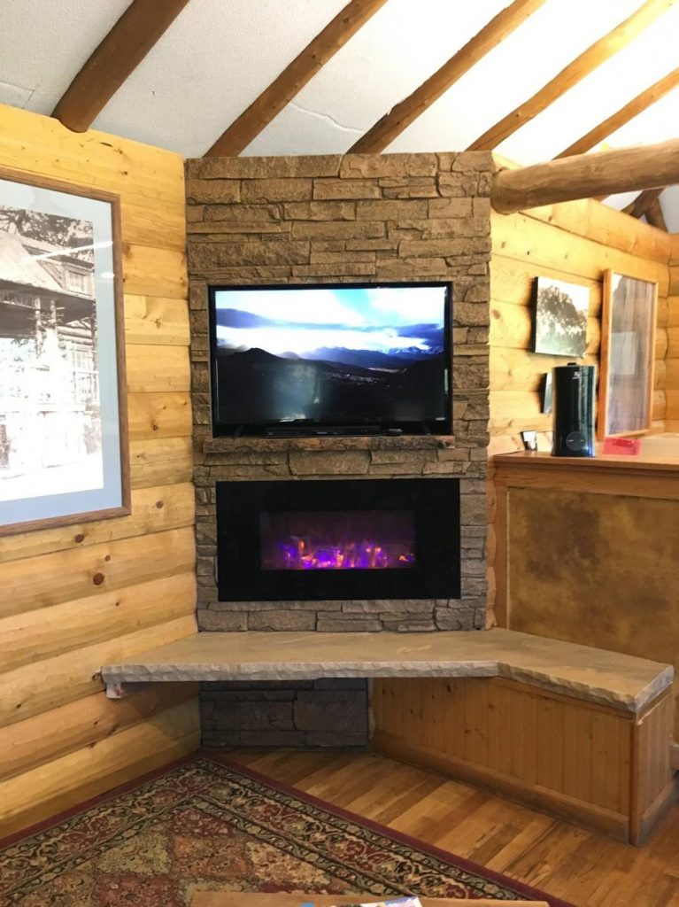 Cozy log cabin fireplace surrounded with Norwich Dakota Stone Wall panels in Toasted Brown.