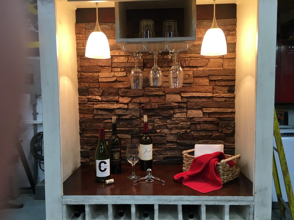 Bar cabinet built from an old TV armoire with wine racks, brushed nickle lights and faux stone panels.