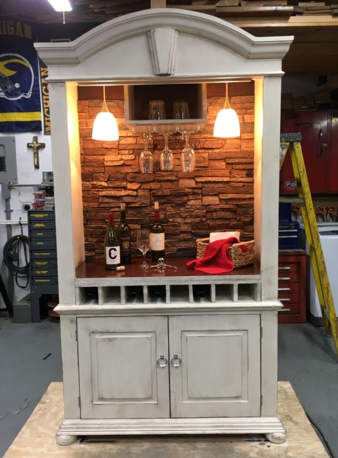 Armoire re-purposed as a bar cabinet with a stone-style back wall.