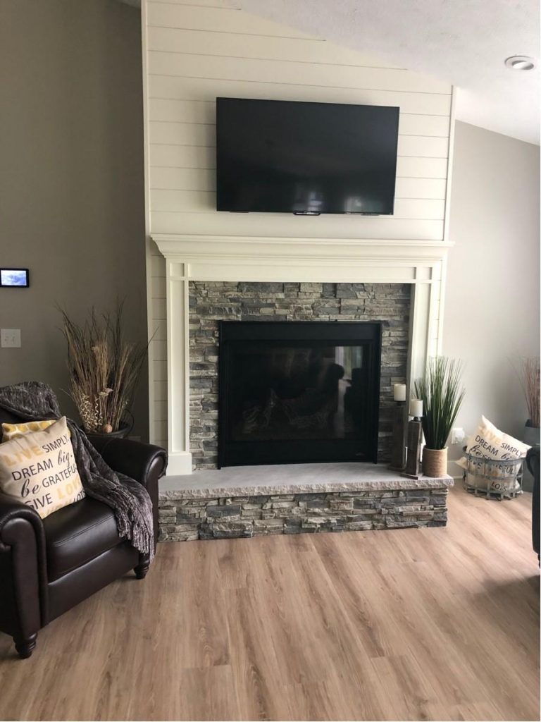 Fireplace with shiplap wall and stacked stone style panels covering the surround and hearth.