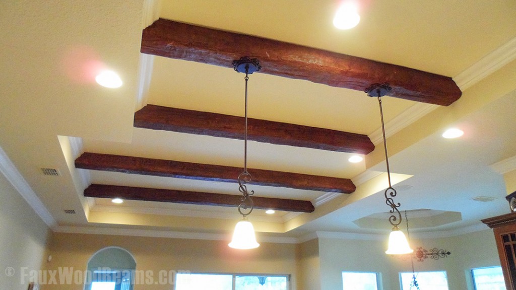 Wood style beams added to a recessed kitchen ceiling with recessed and hanging lights.