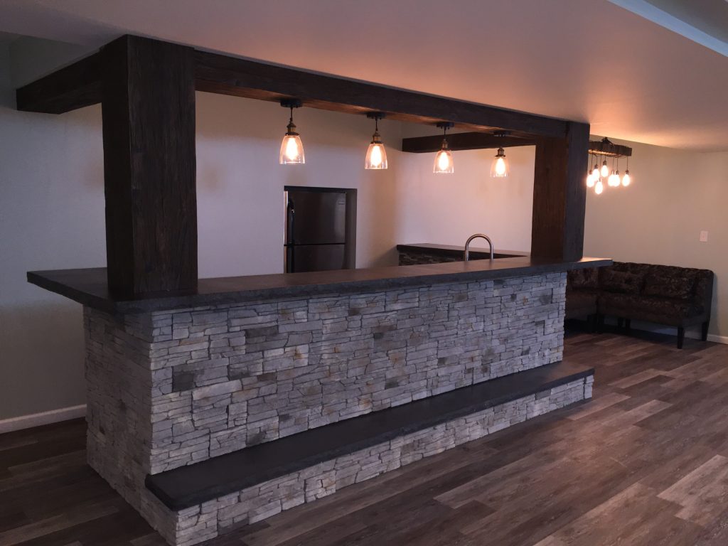 Stunning home basement bar design incorporating faux beams and stone veneer.