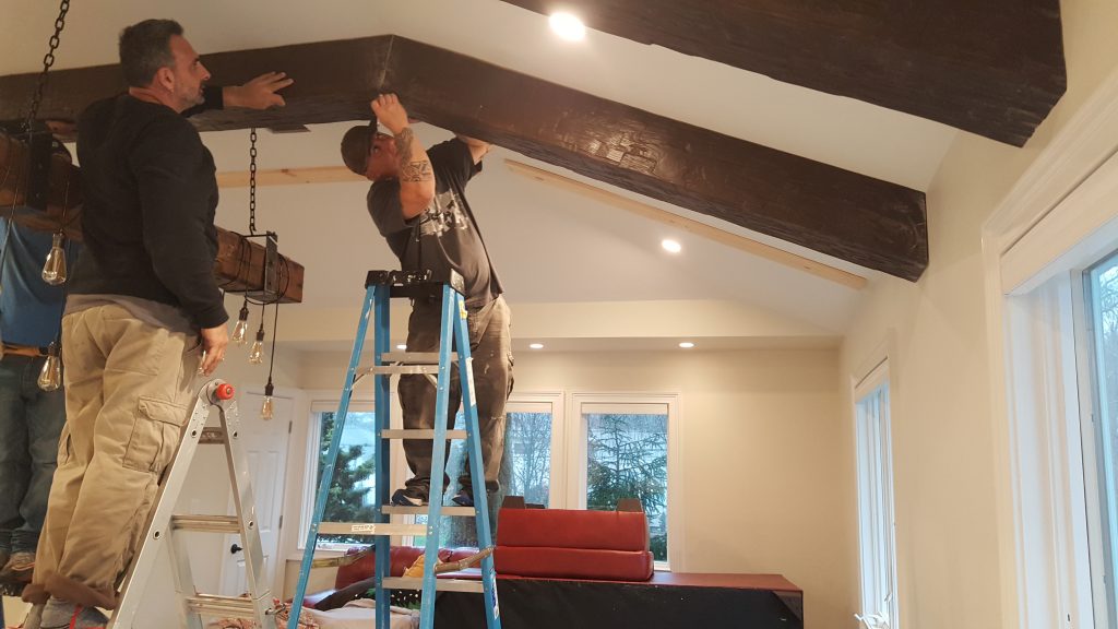 Installing faux beams on a gabled ceiling, mounted on planks and screwed in place.