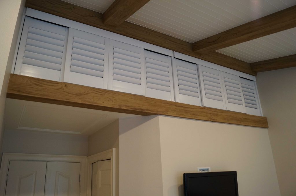 A bedroom's custom cupboards make good use of formerly dead space, and beautifully framed with Driftwood beams.