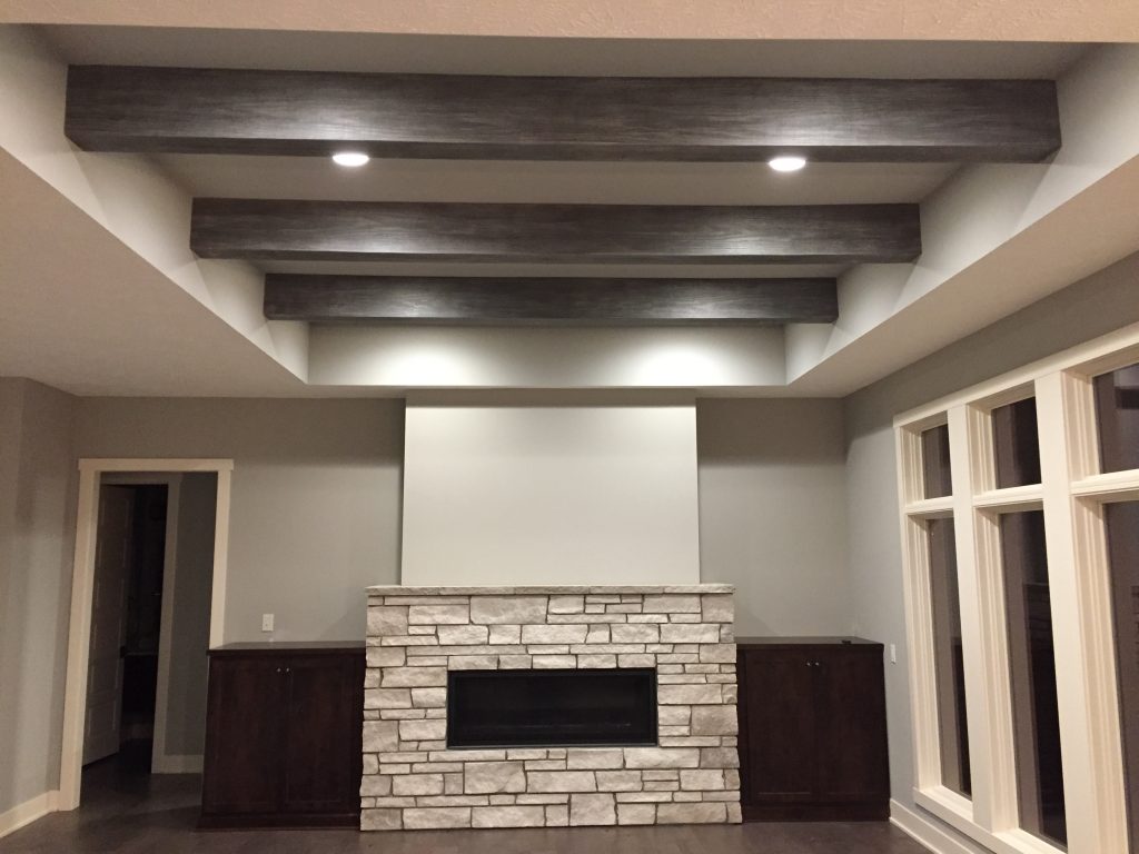 Impressive living room renovation with white stone fireplace and ceiling beams with Gray Patina finish.