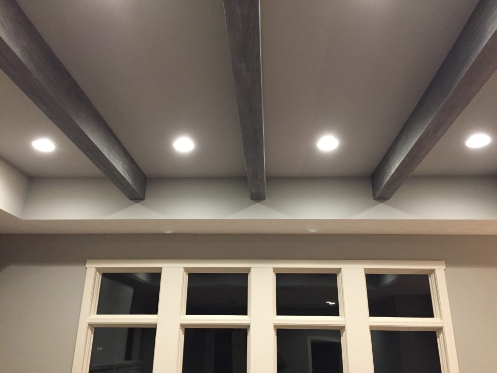 A newly renovated living room with weathered gray beams installed in the recessed ceiling.