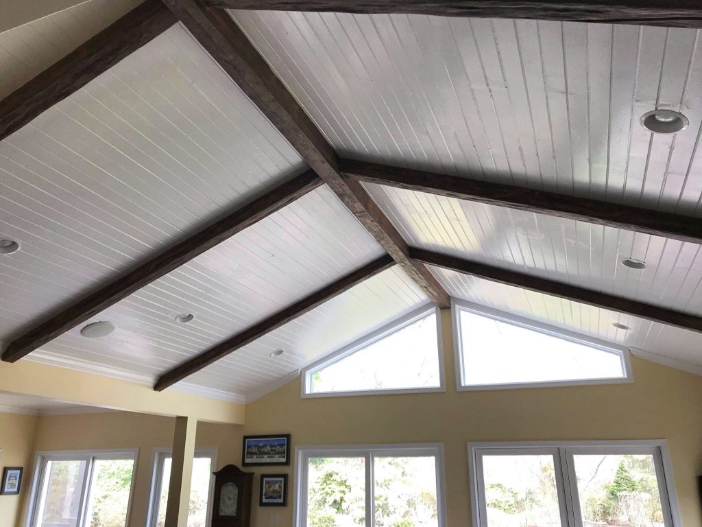 Dark beams installed over a white planked ceiling
