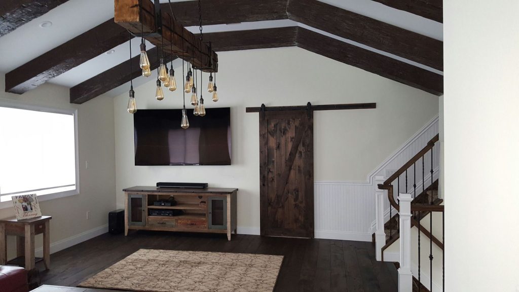 A living room's gabled ceiling made over with Rough Hewn beams and a new light installation.