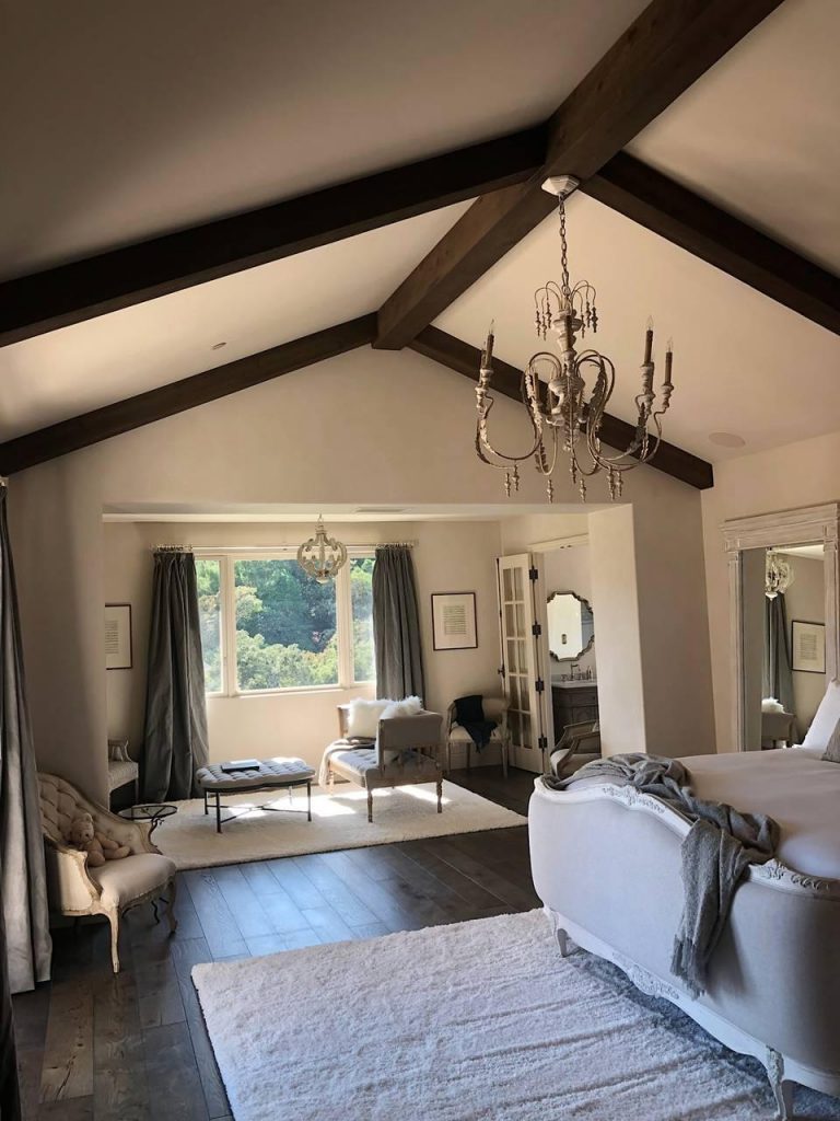 California home's bedroom with elegant furnishings, wrought iron chandelier and exposed decorative beams.