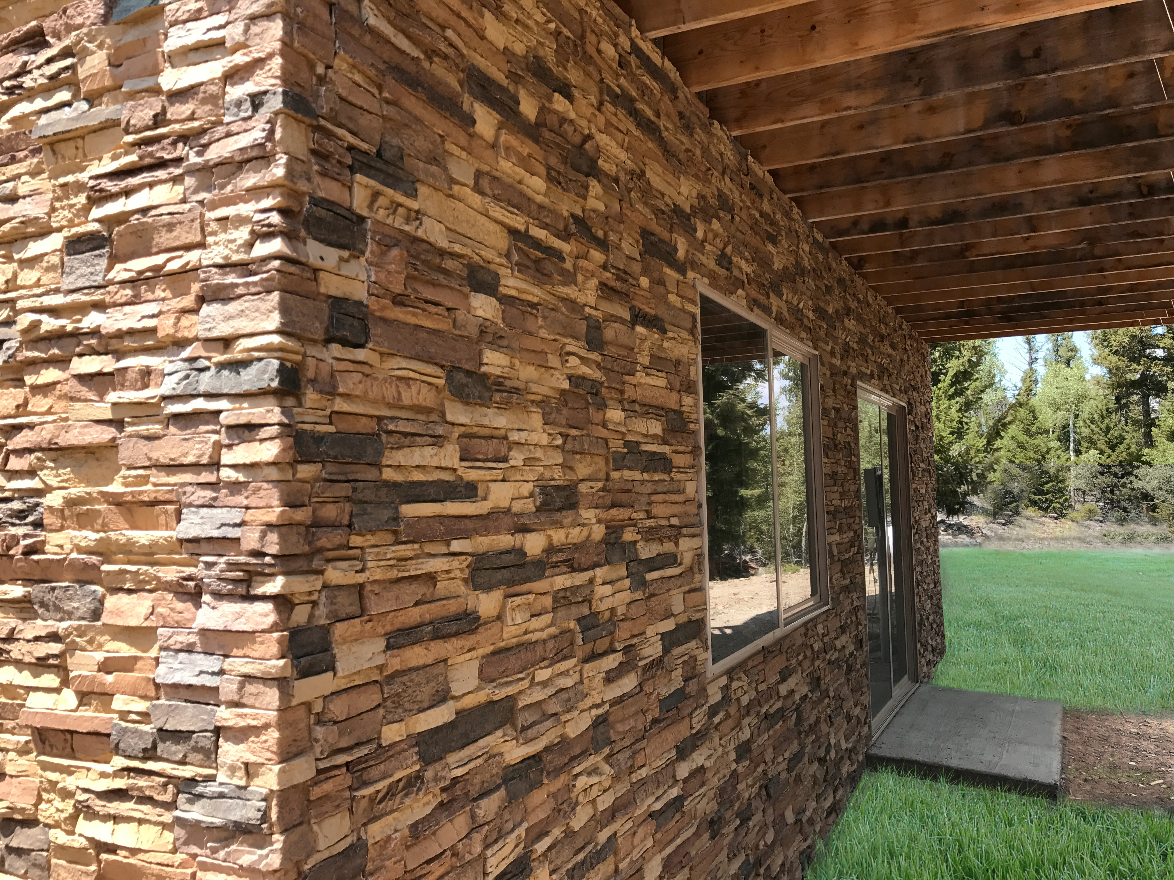 Side of exterior of house with faux stone wall panels, installed around corner.